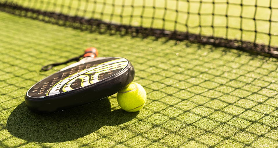 Padelracket en bal op een kunstgras padelbaan naast het net in de zon