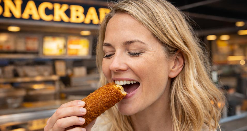 Vrouw neemt een hap van een kroket bij een snackbar